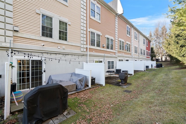 back of property with central AC unit, fence, and a lawn