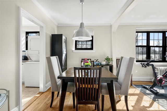 dining room featuring stacked washer and dryer, light wood finished floors, arched walkways, baseboards, and crown molding