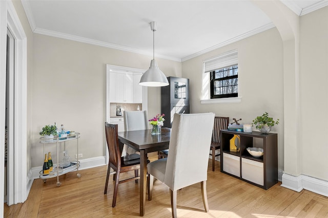 dining space featuring light wood-style floors, arched walkways, and crown molding