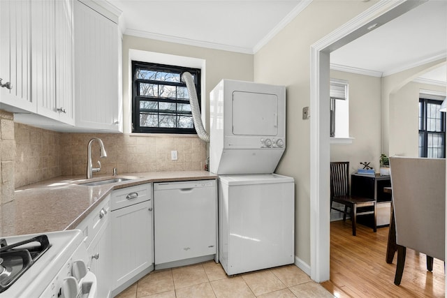 laundry area with stacked washer and dryer, light tile patterned floors, laundry area, crown molding, and a sink