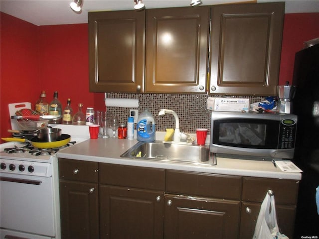 kitchen featuring stainless steel microwave, a sink, decorative backsplash, white gas range, and light countertops