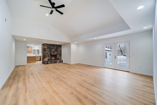 unfurnished living room featuring french doors, ceiling fan, a stone fireplace, light wood-type flooring, and baseboards