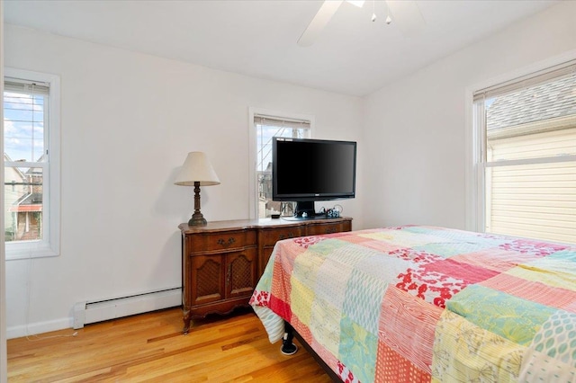bedroom with baseboard heating, a ceiling fan, multiple windows, and light wood-style floors