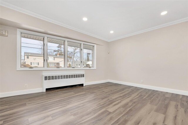 empty room featuring ornamental molding, radiator heating unit, light wood-style flooring, and baseboards