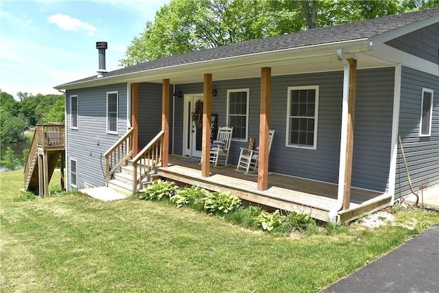 back of house with covered porch, a shingled roof, and a lawn