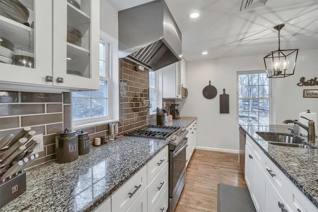 kitchen featuring a sink, white cabinetry, range hood, stainless steel gas stove, and glass insert cabinets