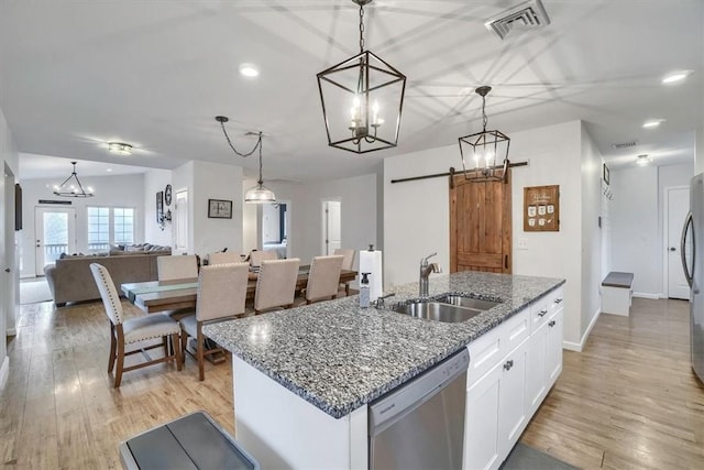 kitchen featuring a barn door, stainless steel appliances, white cabinets, open floor plan, and hanging light fixtures