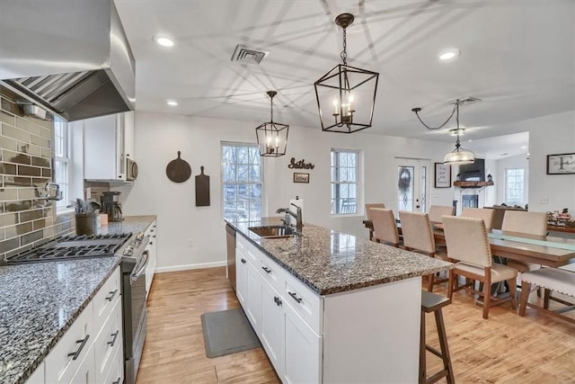 kitchen with an island with sink, dark stone countertops, island exhaust hood, stainless steel appliances, and pendant lighting