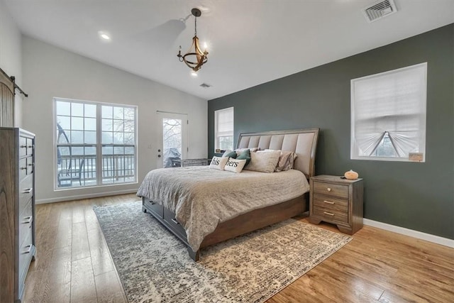 bedroom featuring lofted ceiling, a barn door, visible vents, and wood finished floors