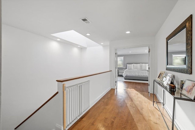 hall featuring a skylight, visible vents, light wood-style flooring, an upstairs landing, and recessed lighting