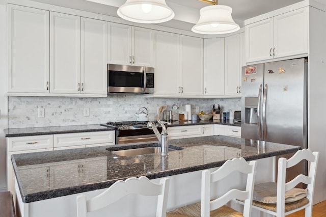 kitchen with appliances with stainless steel finishes, an island with sink, decorative light fixtures, and a kitchen breakfast bar