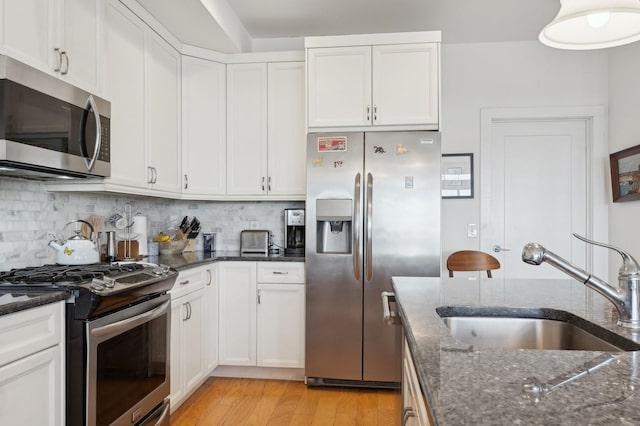 kitchen featuring a sink, white cabinetry, appliances with stainless steel finishes, dark stone counters, and tasteful backsplash