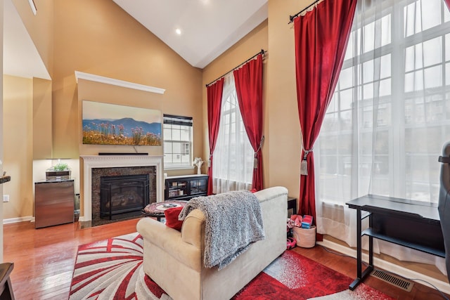 living room featuring a fireplace, visible vents, wood finished floors, high vaulted ceiling, and baseboards