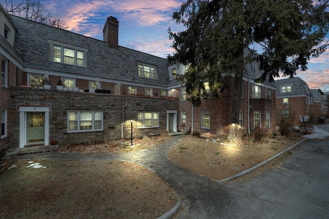 exterior space with a high end roof, stone siding, brick siding, and a chimney