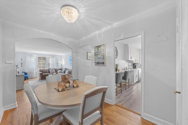 dining room with light wood-style floors, baseboards, arched walkways, and an inviting chandelier