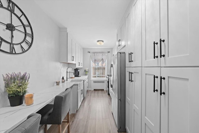 kitchen with white cabinets, radiator heating unit, light stone counters, freestanding refrigerator, and a sink