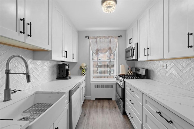 kitchen with radiator, appliances with stainless steel finishes, white cabinetry, a sink, and wood finished floors