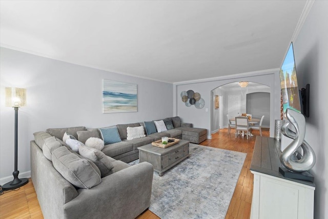 living room with light wood-style floors, arched walkways, crown molding, and baseboards