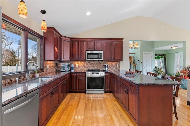 kitchen featuring a breakfast bar area, decorative light fixtures, a peninsula, stainless steel appliances, and a sink