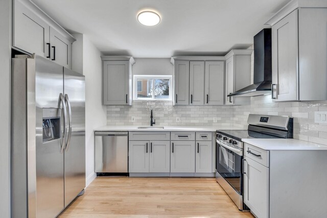 kitchen with light countertops, light wood-style flooring, appliances with stainless steel finishes, a sink, and wall chimney exhaust hood