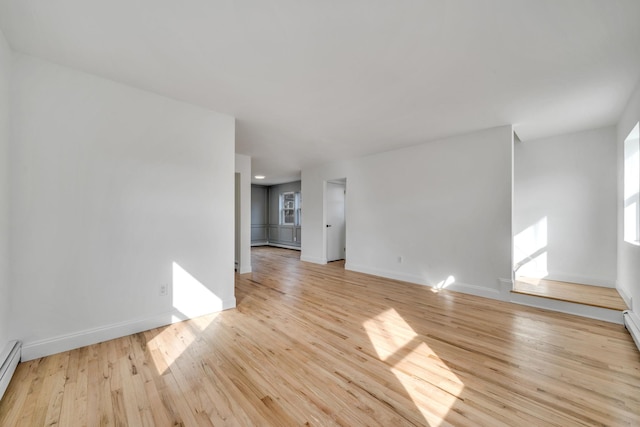 unfurnished room featuring baseboard heating, light wood-style flooring, and baseboards