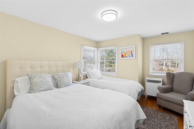 bedroom with radiator heating unit, multiple windows, visible vents, and dark wood-type flooring