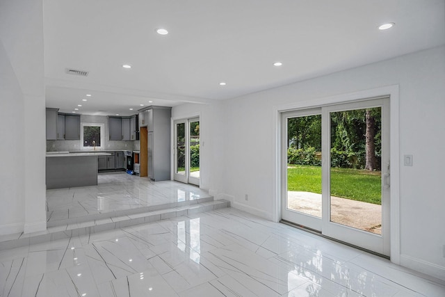 unfurnished living room with marble finish floor, baseboards, visible vents, and a wealth of natural light