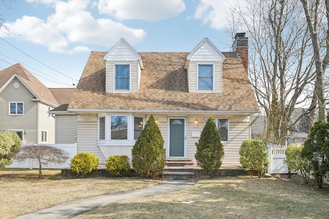 view of front of house with a front yard, roof with shingles, fence, and a chimney