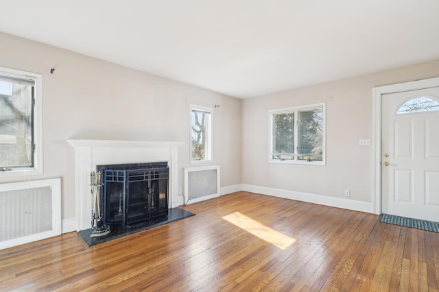 unfurnished living room with a fireplace with raised hearth, wood finished floors, and baseboards