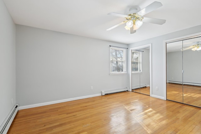 unfurnished bedroom with a baseboard radiator, light wood-style flooring, and two closets