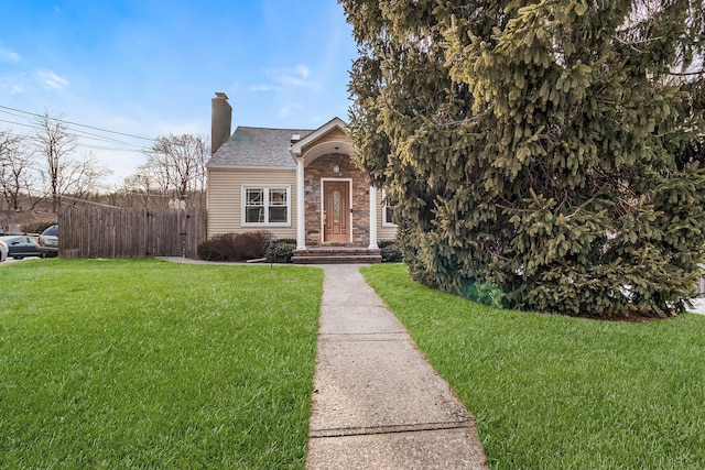 view of front of house with a front yard, stone siding, fence, and a chimney