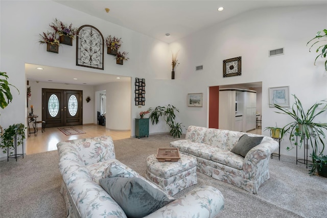 living area featuring visible vents, light carpet, and a high ceiling