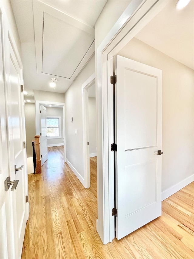 corridor featuring baseboards, attic access, and light wood finished floors