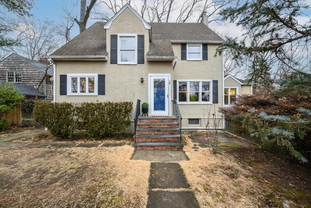 view of front of home with a shingled roof, a chimney, fence, and stucco siding