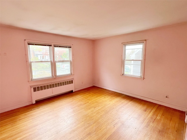 spare room with baseboards, light wood-type flooring, a healthy amount of sunlight, and radiator heating unit