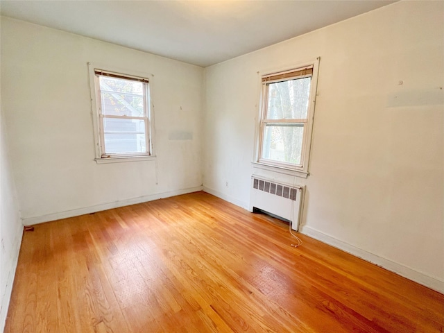 empty room featuring baseboards, radiator, and light wood finished floors