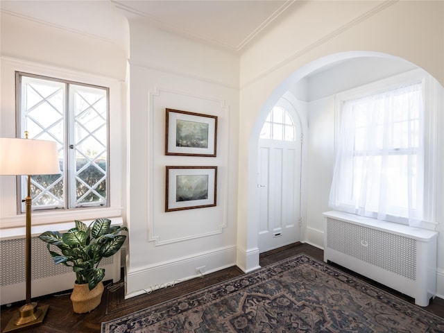 foyer entrance with dark wood-style floors, arched walkways, radiator, ornamental molding, and baseboards