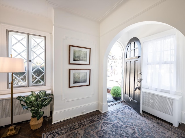 foyer entrance featuring plenty of natural light, radiator heating unit, arched walkways, and crown molding