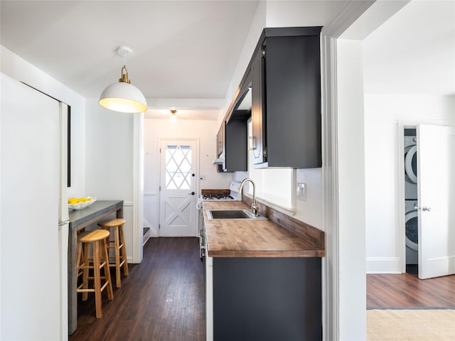 kitchen featuring dark wood-style flooring, stacked washer / dryer, wood counters, dark cabinetry, and pendant lighting