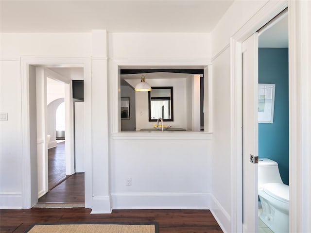 corridor with radiator heating unit, dark wood-style flooring, a sink, and baseboards