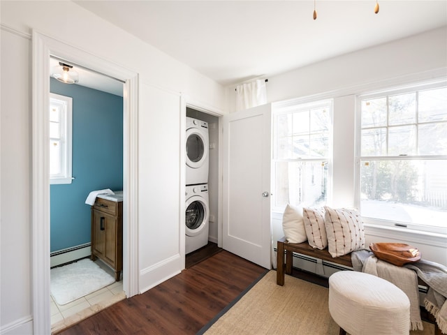 clothes washing area featuring stacked washer / dryer, laundry area, a healthy amount of sunlight, and wood finished floors