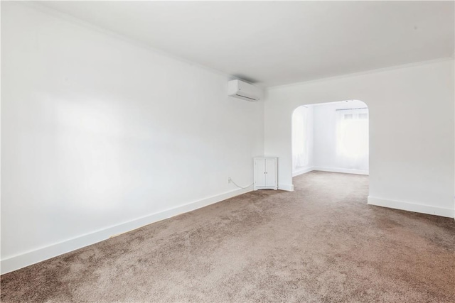 empty room featuring arched walkways, a wall unit AC, carpet flooring, baseboards, and ornamental molding