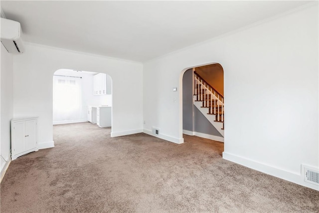 carpeted empty room featuring arched walkways, a wall mounted air conditioner, visible vents, and baseboards