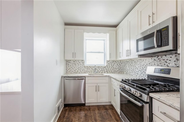 kitchen featuring appliances with stainless steel finishes, white cabinets, light stone counters, and dark wood-style floors