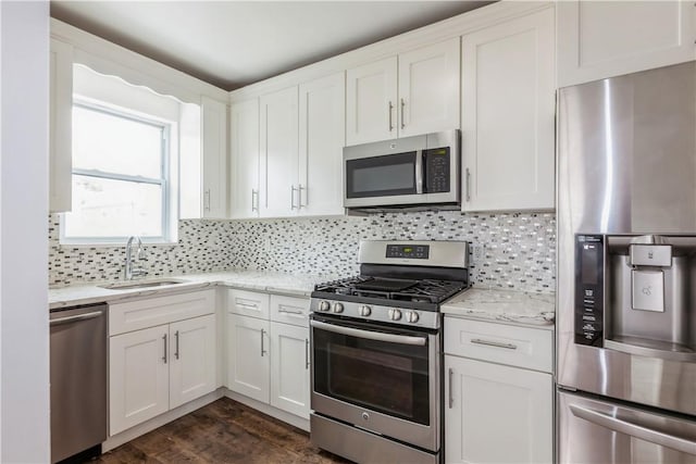 kitchen with a sink, white cabinets, appliances with stainless steel finishes, backsplash, and light stone countertops