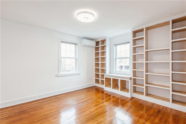 empty room featuring a wall unit AC, wood finished floors, and baseboards