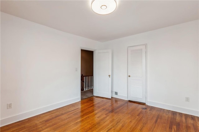 empty room featuring wood finished floors, visible vents, and baseboards