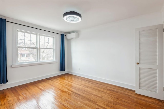 unfurnished room with light wood-type flooring, baseboards, and an AC wall unit