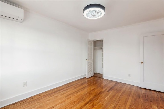 unfurnished bedroom with a closet, baseboards, wood finished floors, and a wall mounted air conditioner