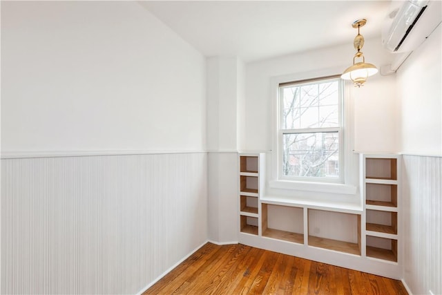 interior space featuring a wall mounted air conditioner, wainscoting, and wood finished floors